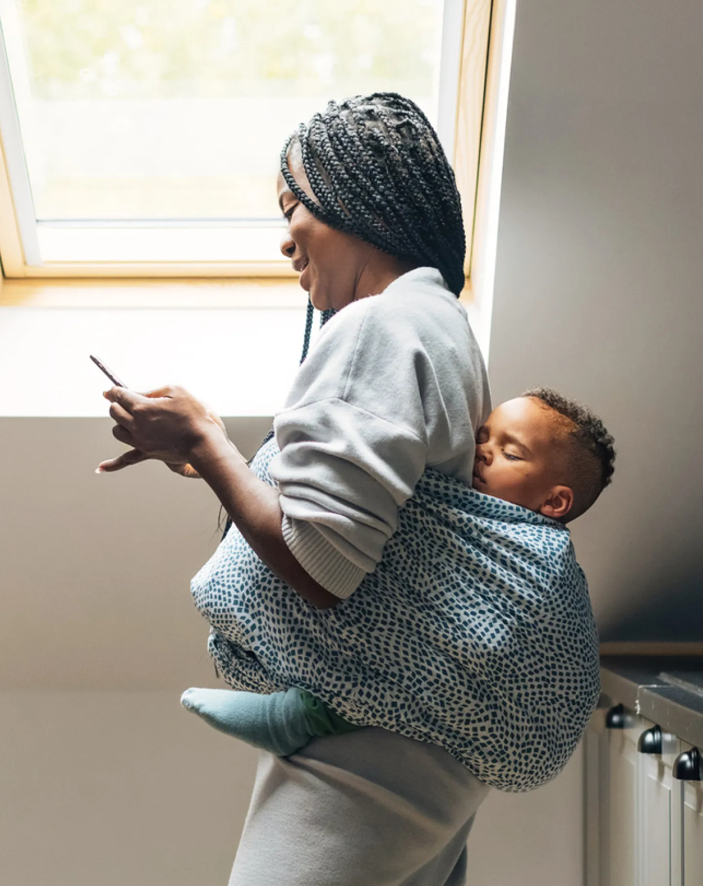 A woman carrying a child on her back and holding a phone in her hand